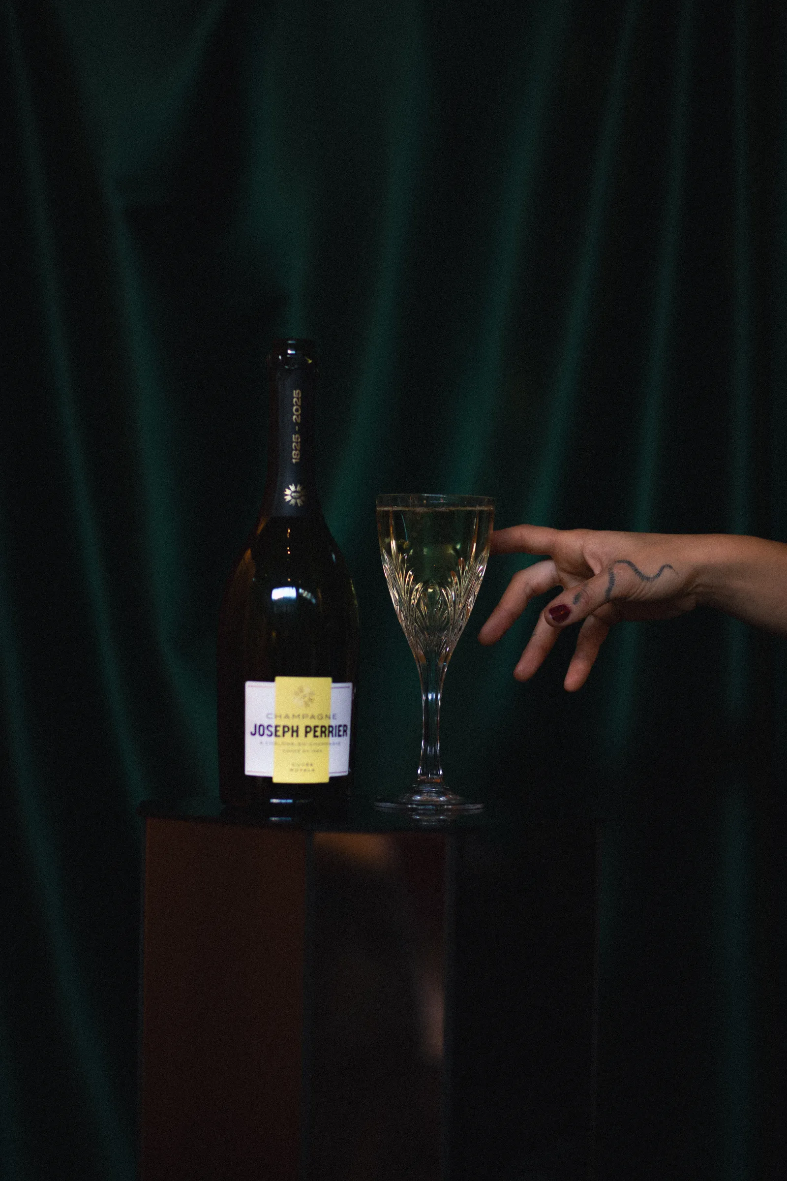 Fles Joseph Perrier champagne en een kristallen glas voor een groen gordijn